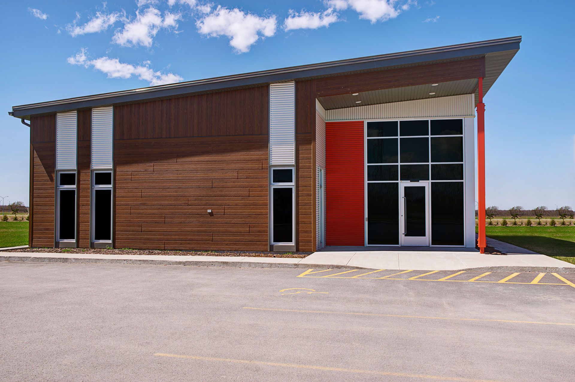 Modern, brown building with a red accent door and large glass windows; blue sky background.