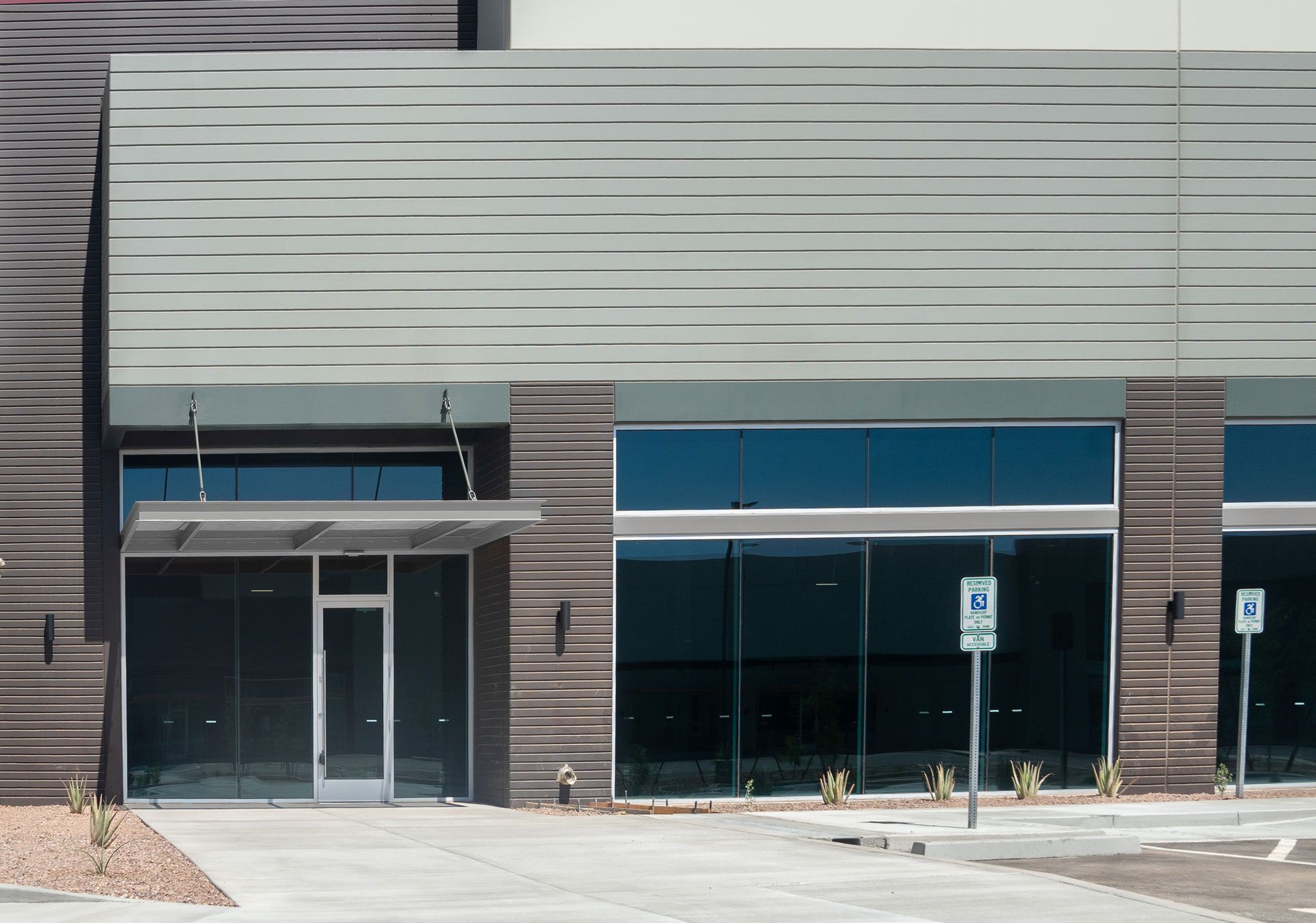 Modern commercial building with glass windows, gray and brown panels, and a concrete entrance.