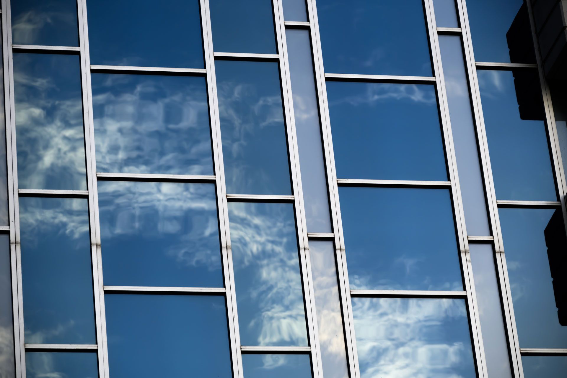 Blue sky and clouds reflected in a grid of windows on a modern building.