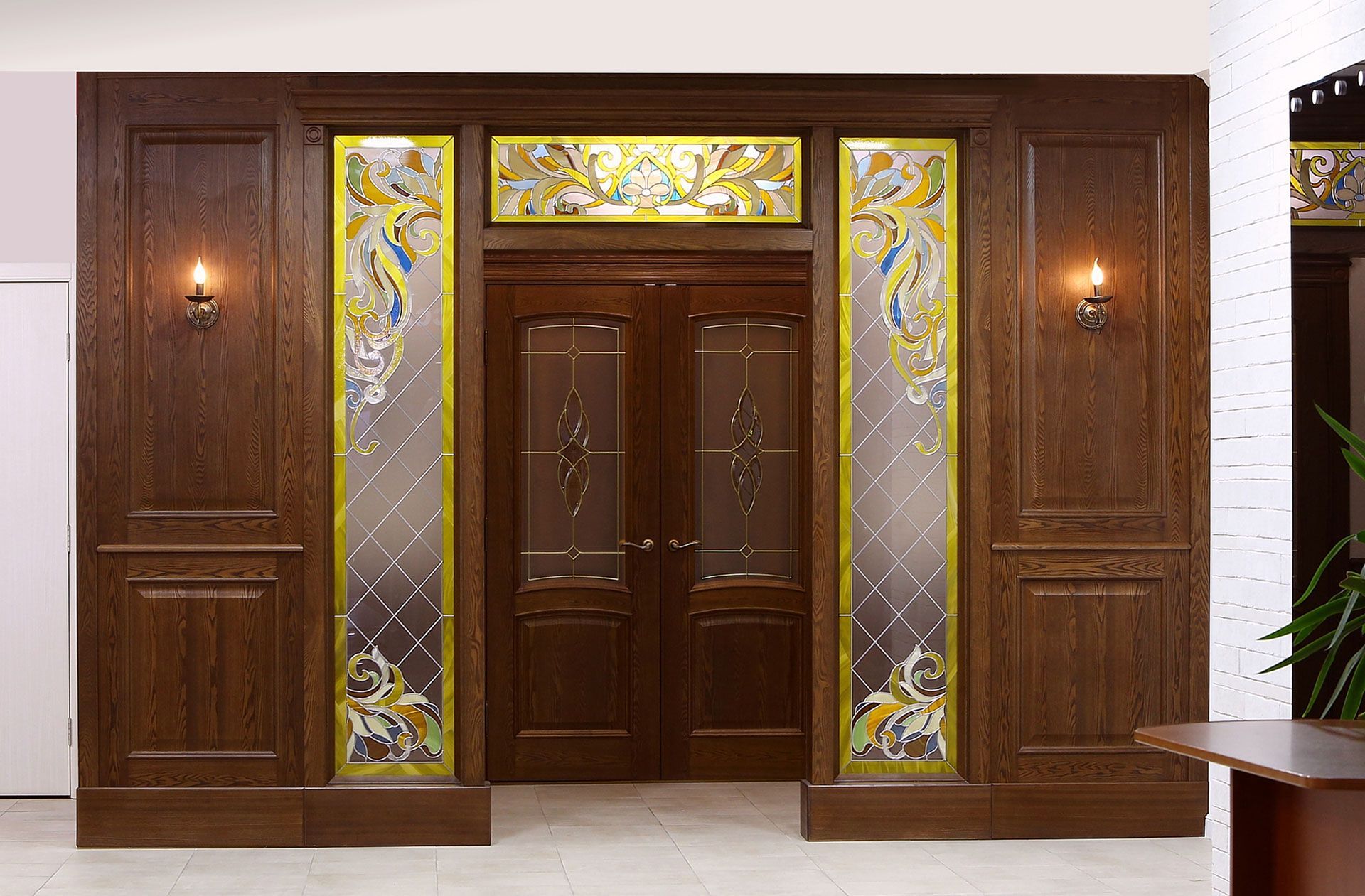 Wooden door with decorative stained-glass panels and sconce lighting.