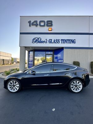 White car with tinted windows parked outside Blue's Glass Tinting shop. Blue signage and building number 1408 are visible.