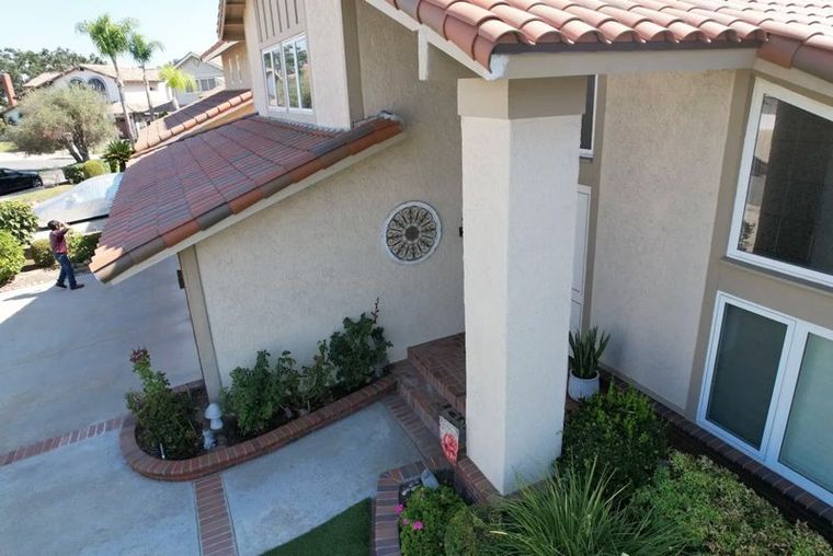 An angled, eye-level view of a house entrance with beige stucco walls, a brown tile roof, and a white support column.
