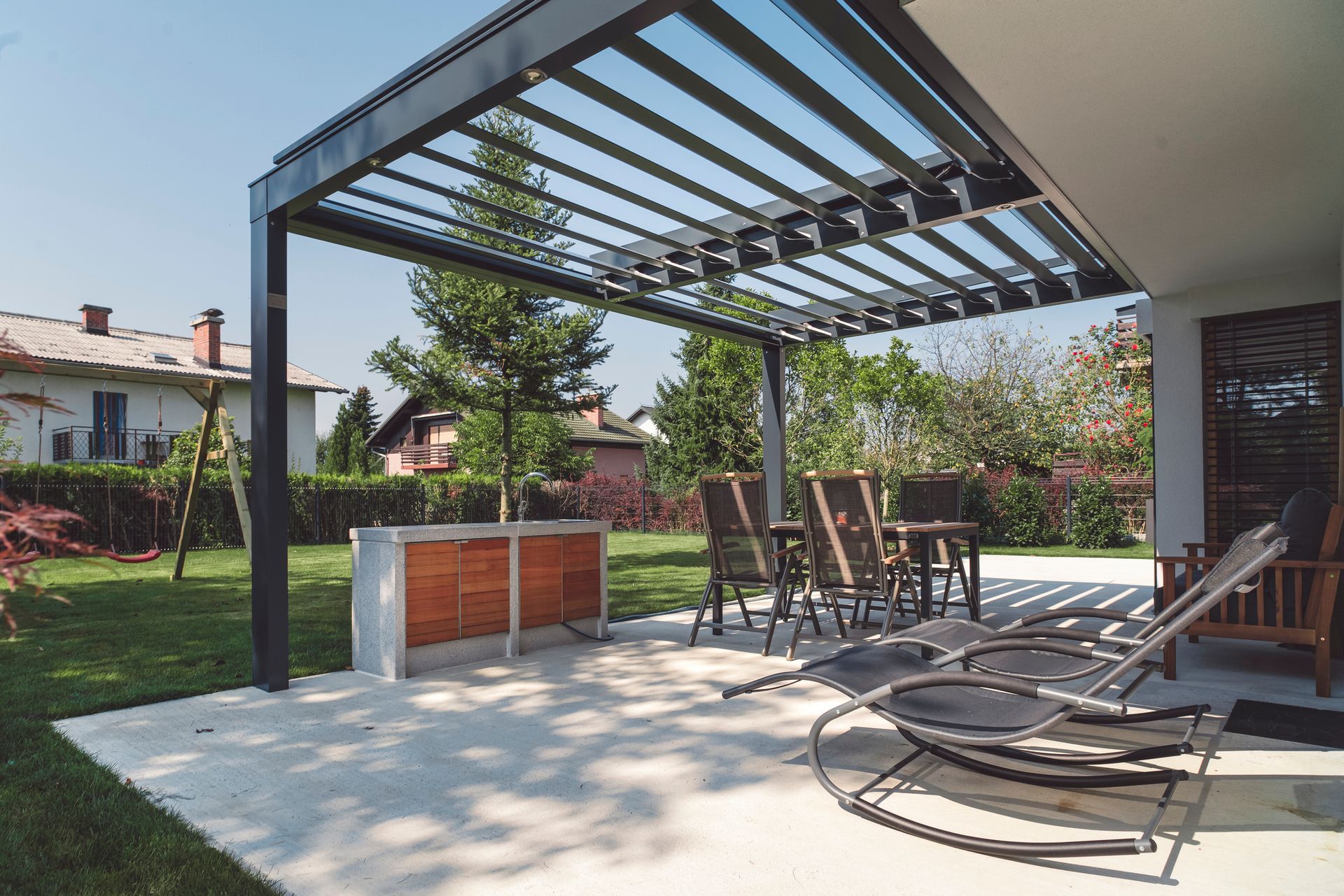 Modern patio with custom concrete flooring, outdoor kitchen, and pergola in landscaped backyard.