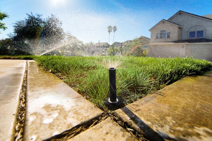 A sprinkler is spraying water on a lush green lawn in front of a house.