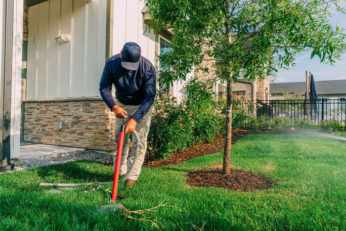 A man is watering a lawn with a hose in front of a house.