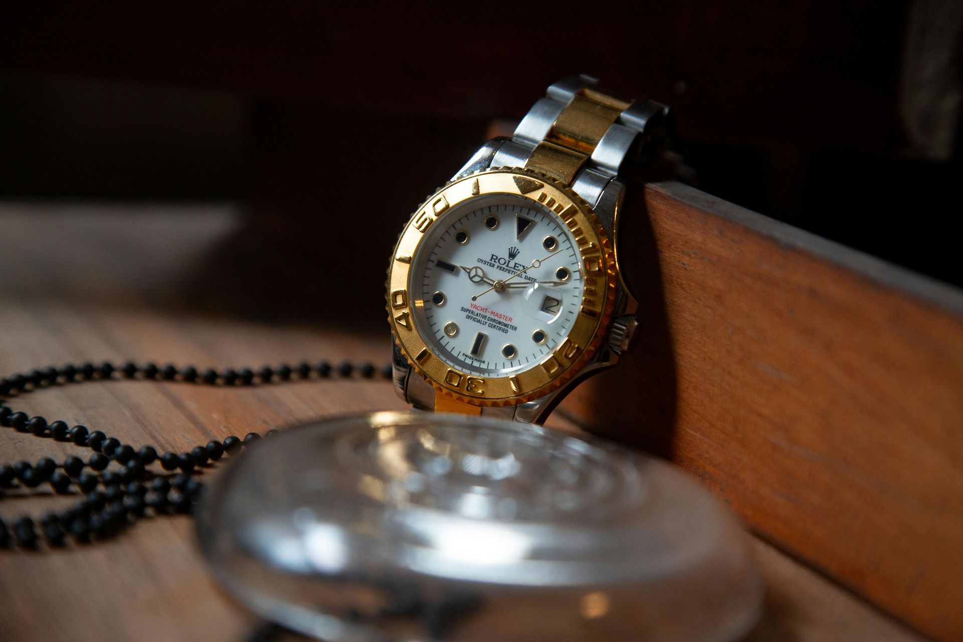 Two-tone Rolex watch, silver chain, and silver disc on wooden surface.