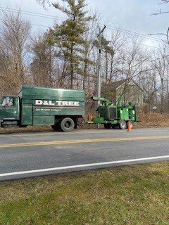 A green truck is parked on the side of the road next to a tree chipper.