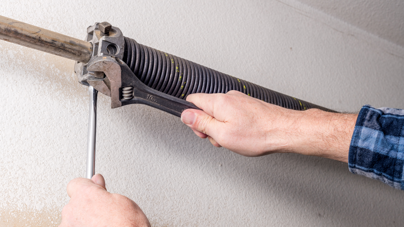 A man is fixing a garage door spring with a wrench.