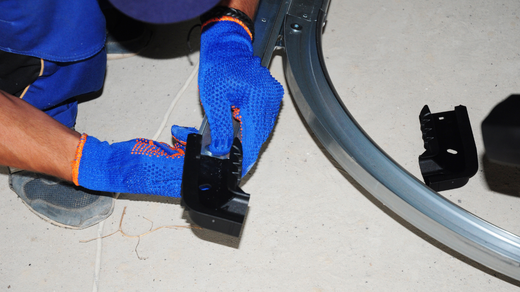 A man wearing blue gloves is working on a garage door.