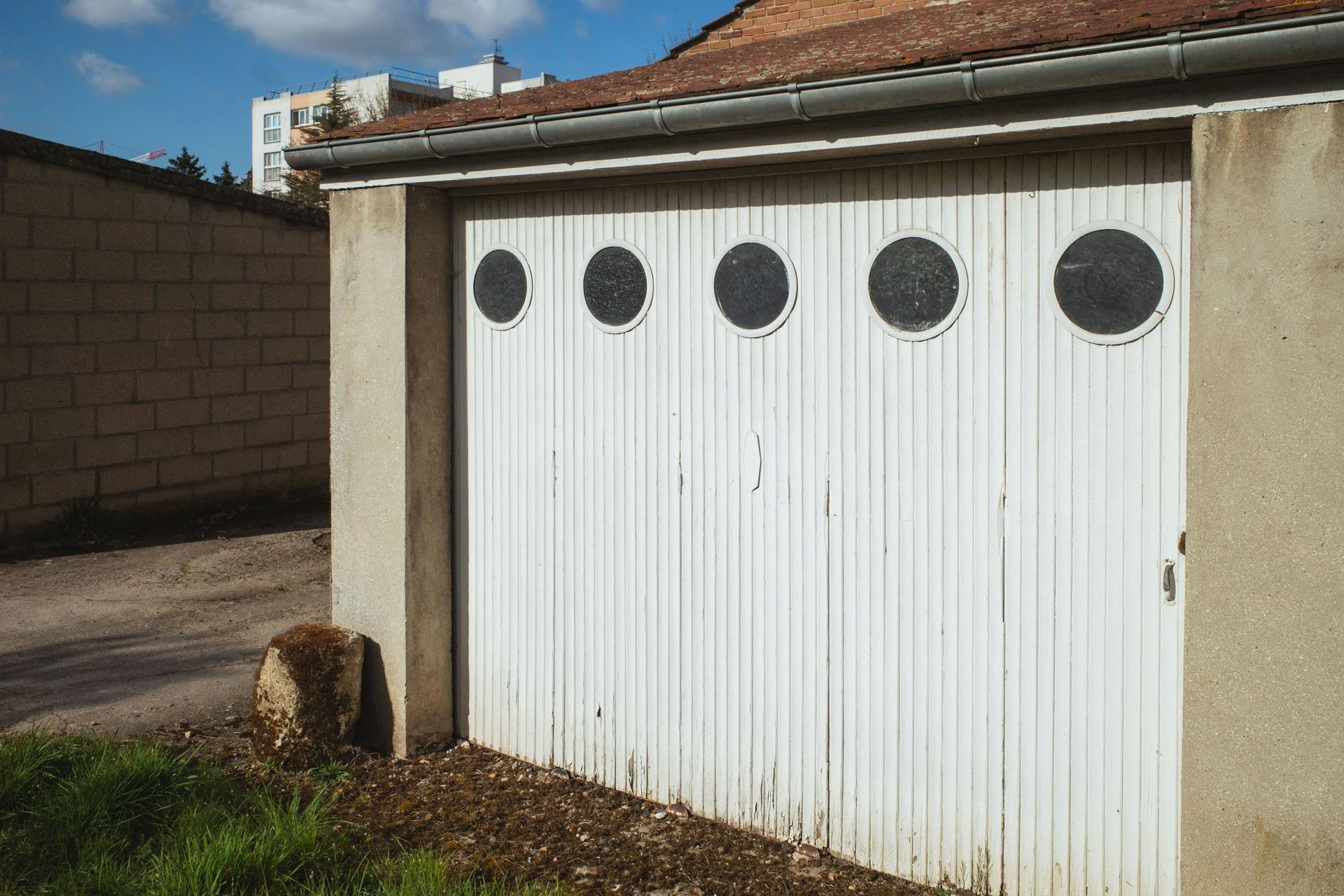 White garage door with five round black windows, tan trim, and a brick wall to the side.