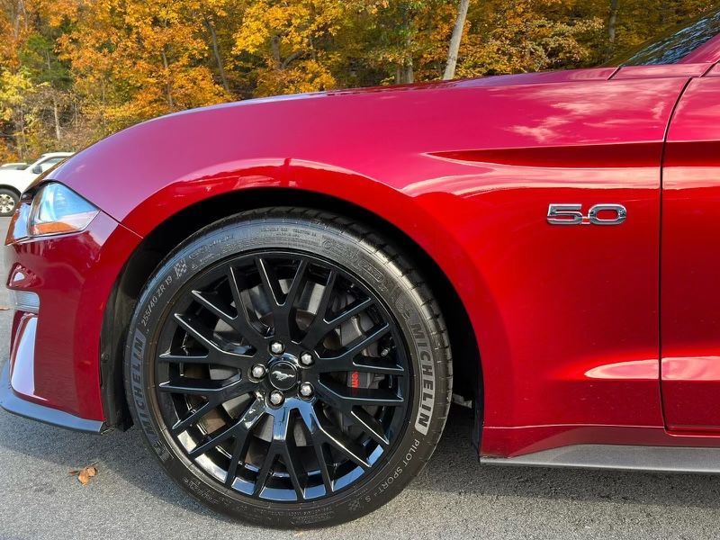 A red ford mustang with black wheels is parked in a parking lot.