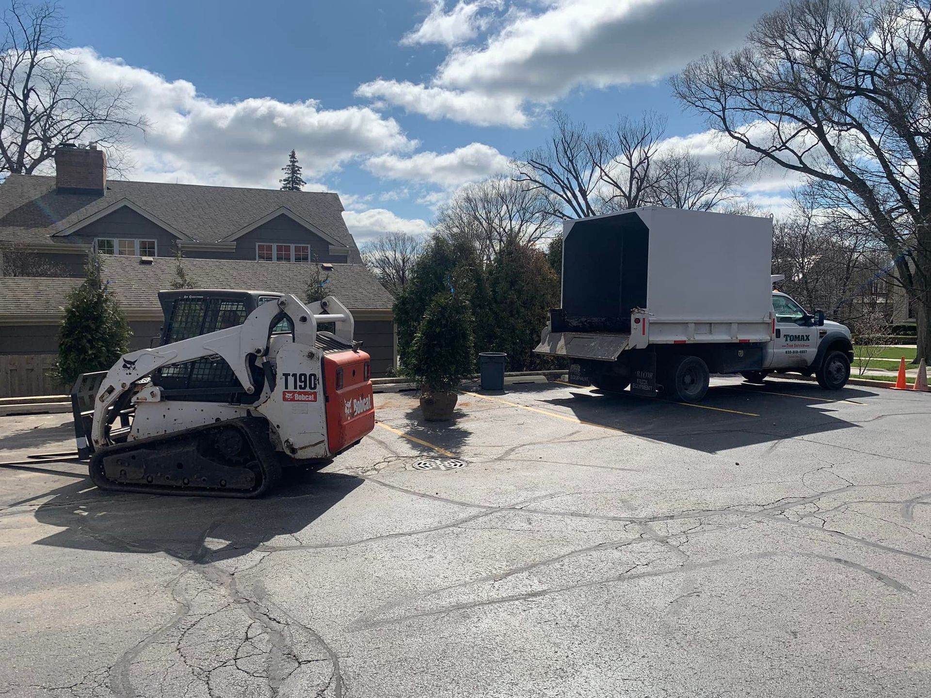 A bulldozer and a truck are parked in a parking lot in front of a house.