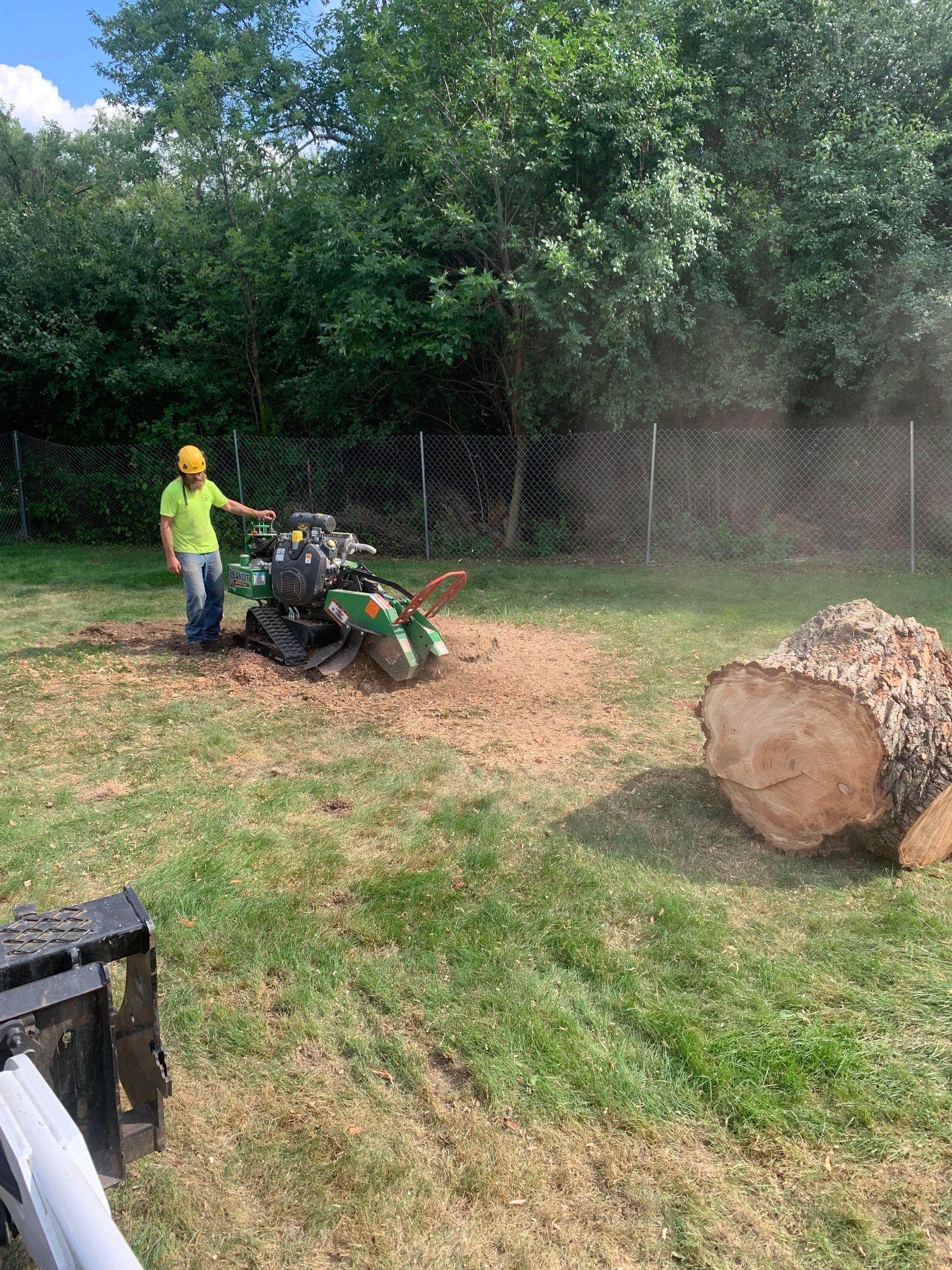 A man is standing next to a stump grinder in a yard.