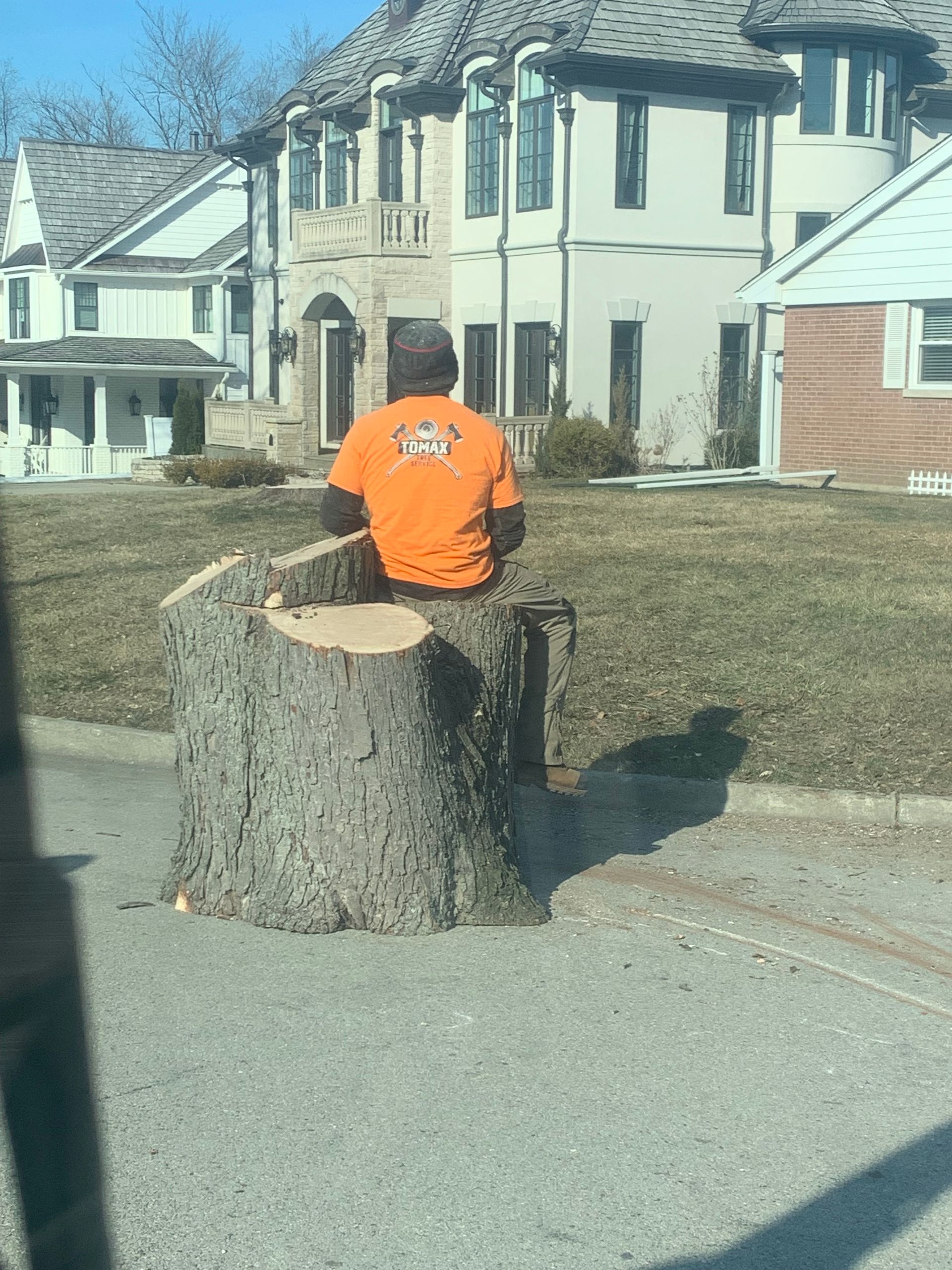 A man is sitting on a tree stump in front of a house.