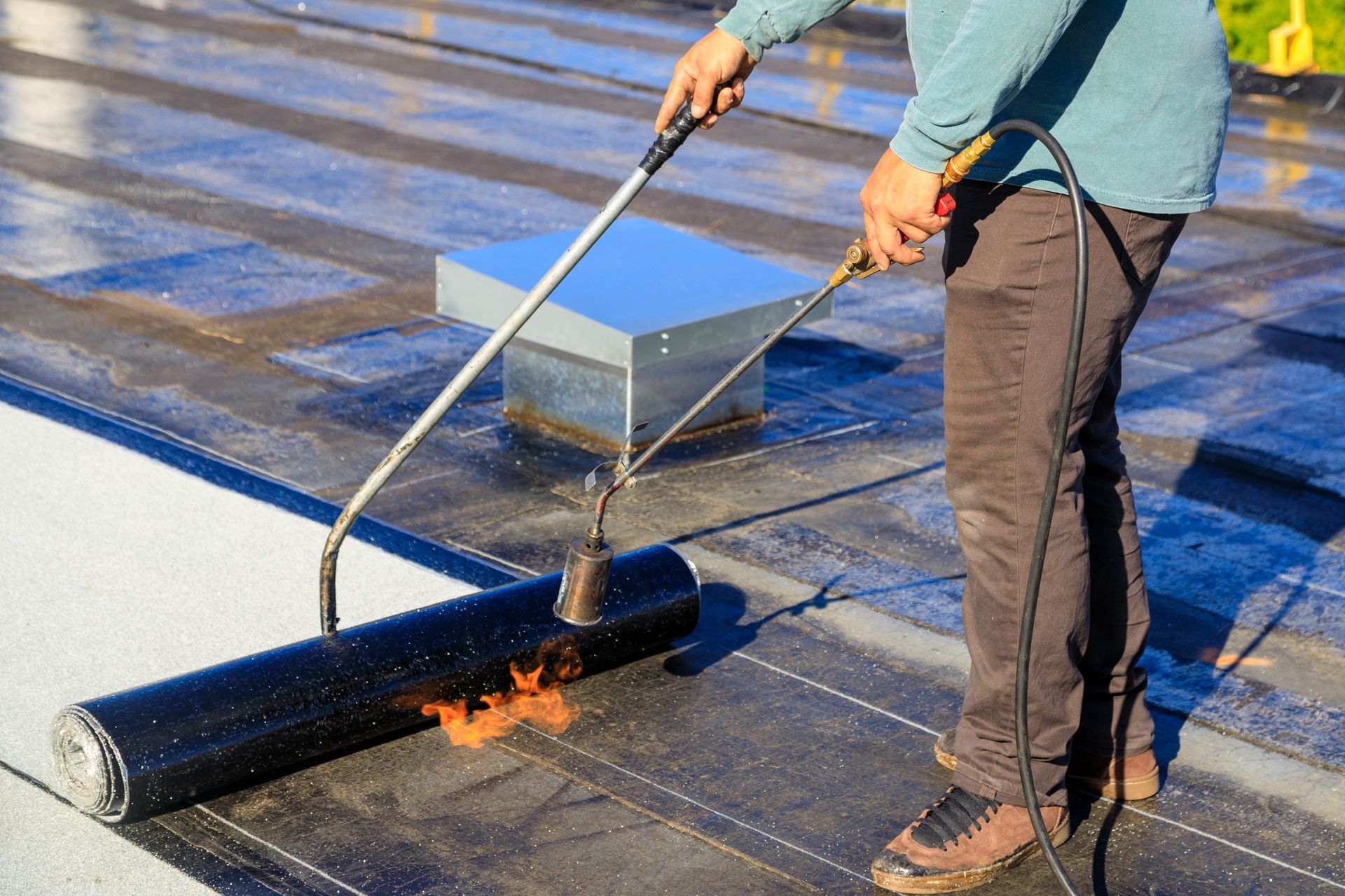 Person using a torch to install roofing material on a flat roof.