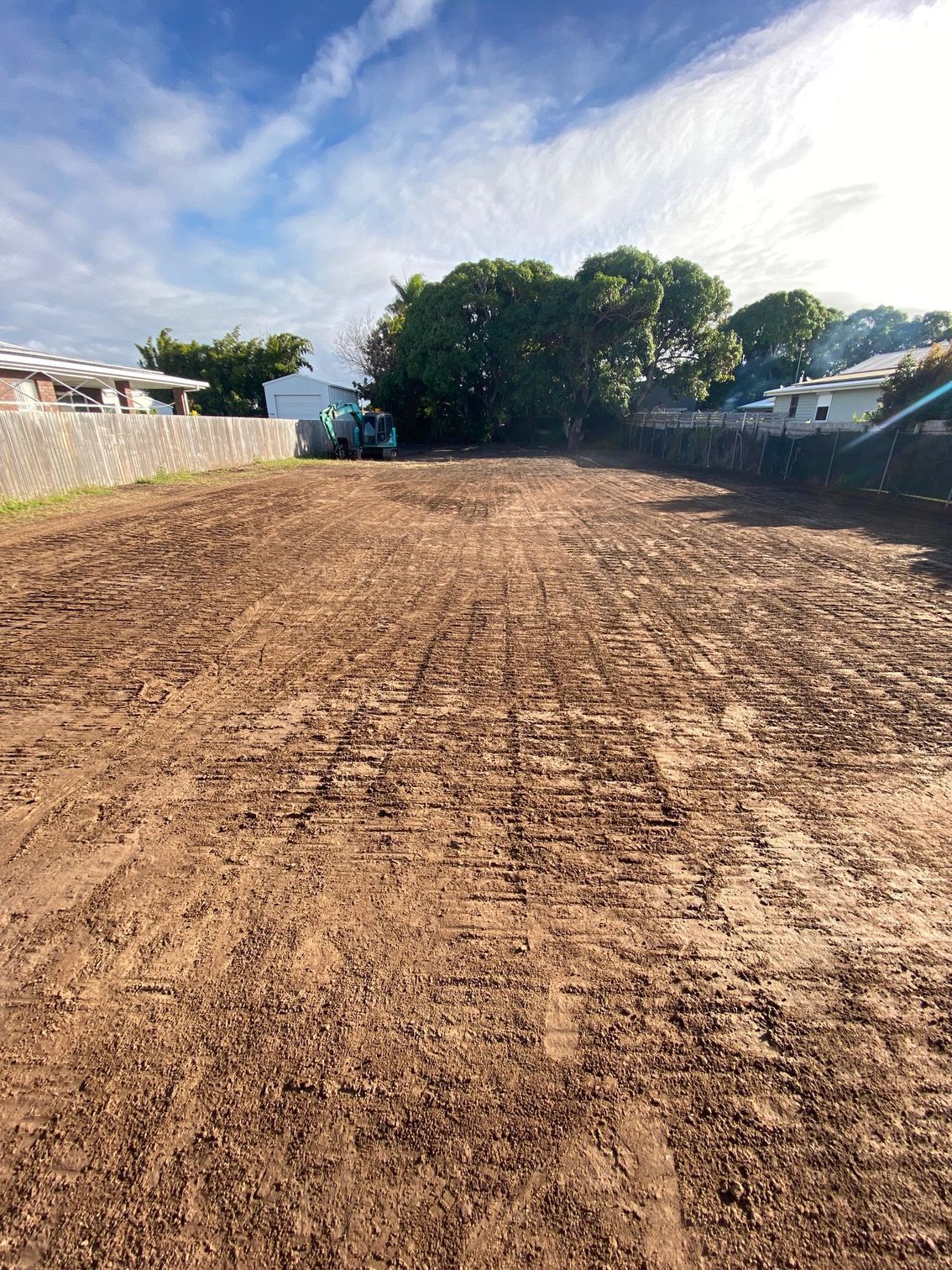 Cleared dirt lot ready for construction, with trees and houses in the background under a blue sky — Integrabuild in Airlie Beach, QLD