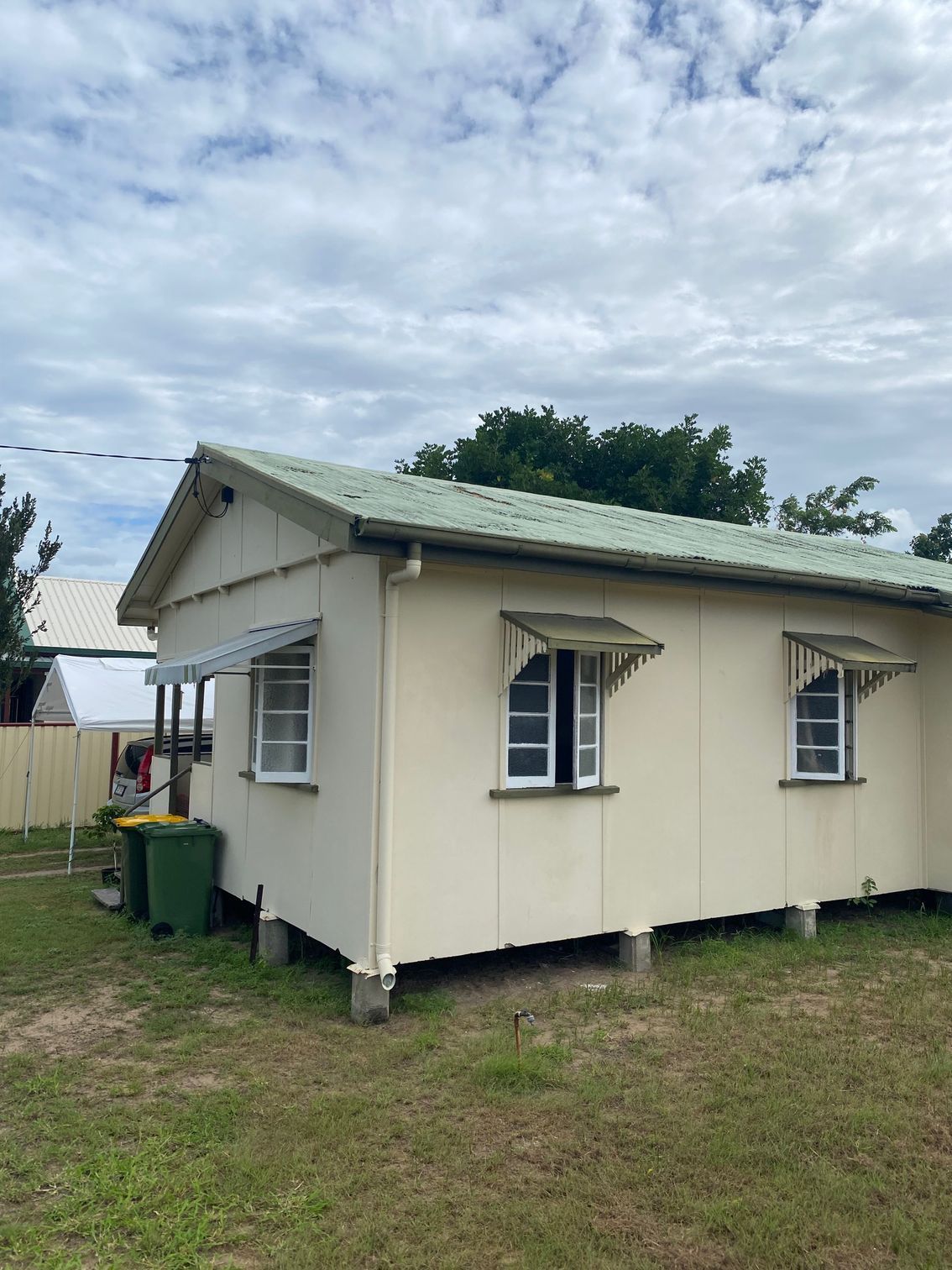 Tan cottage with green roof and awnings, set on pillars, cloudy sky overhead — Integrabuild in Airlie Beach, QLD