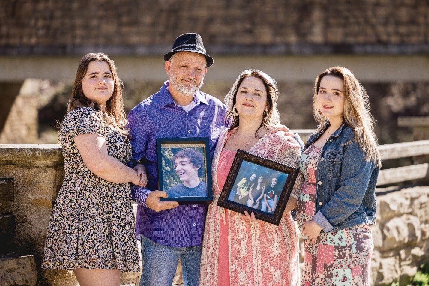 Family outdoors holding framed photos of loved ones.