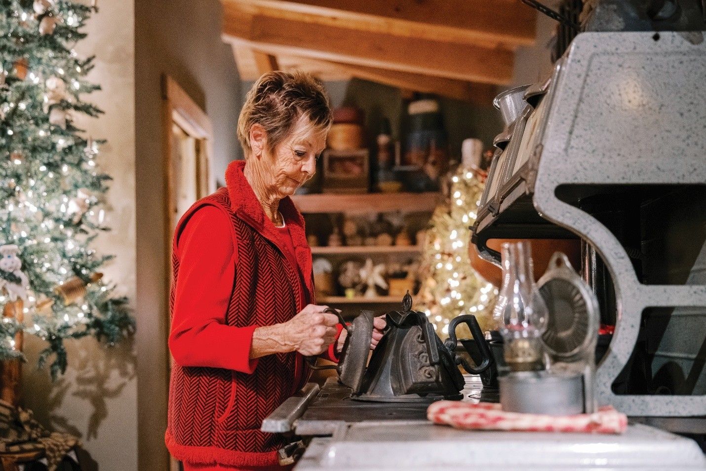Woman in red vest near an antique saw, Christmas tree visible in background.