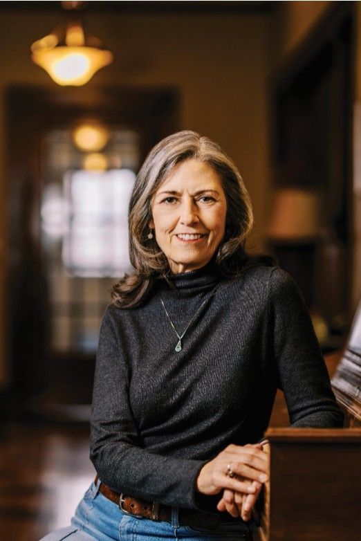 Woman in a dark turtleneck and jeans smiles in a room with a piano.