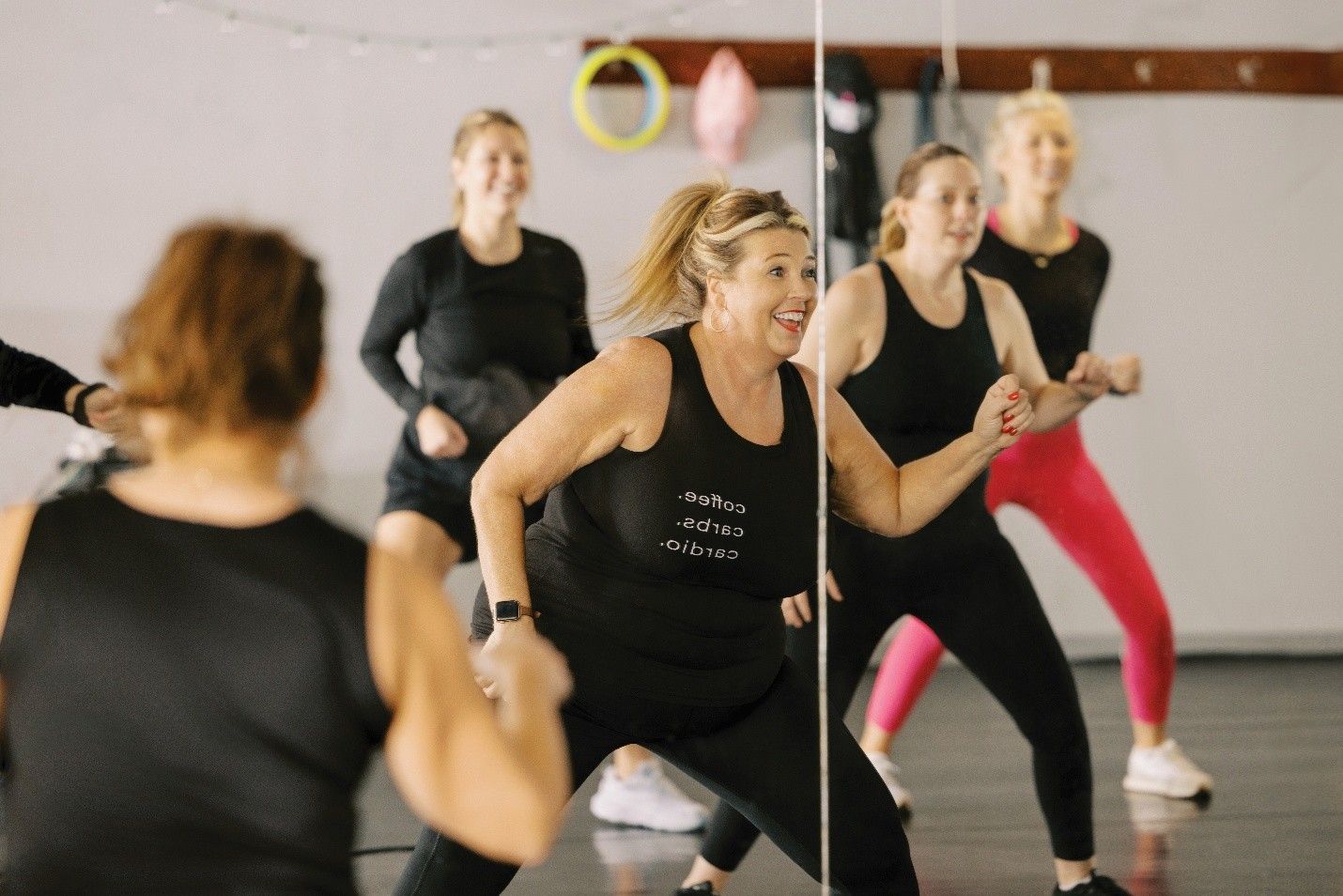 Women in a dance class, mirror reflecting their movements; wearing workout clothes, indoors.