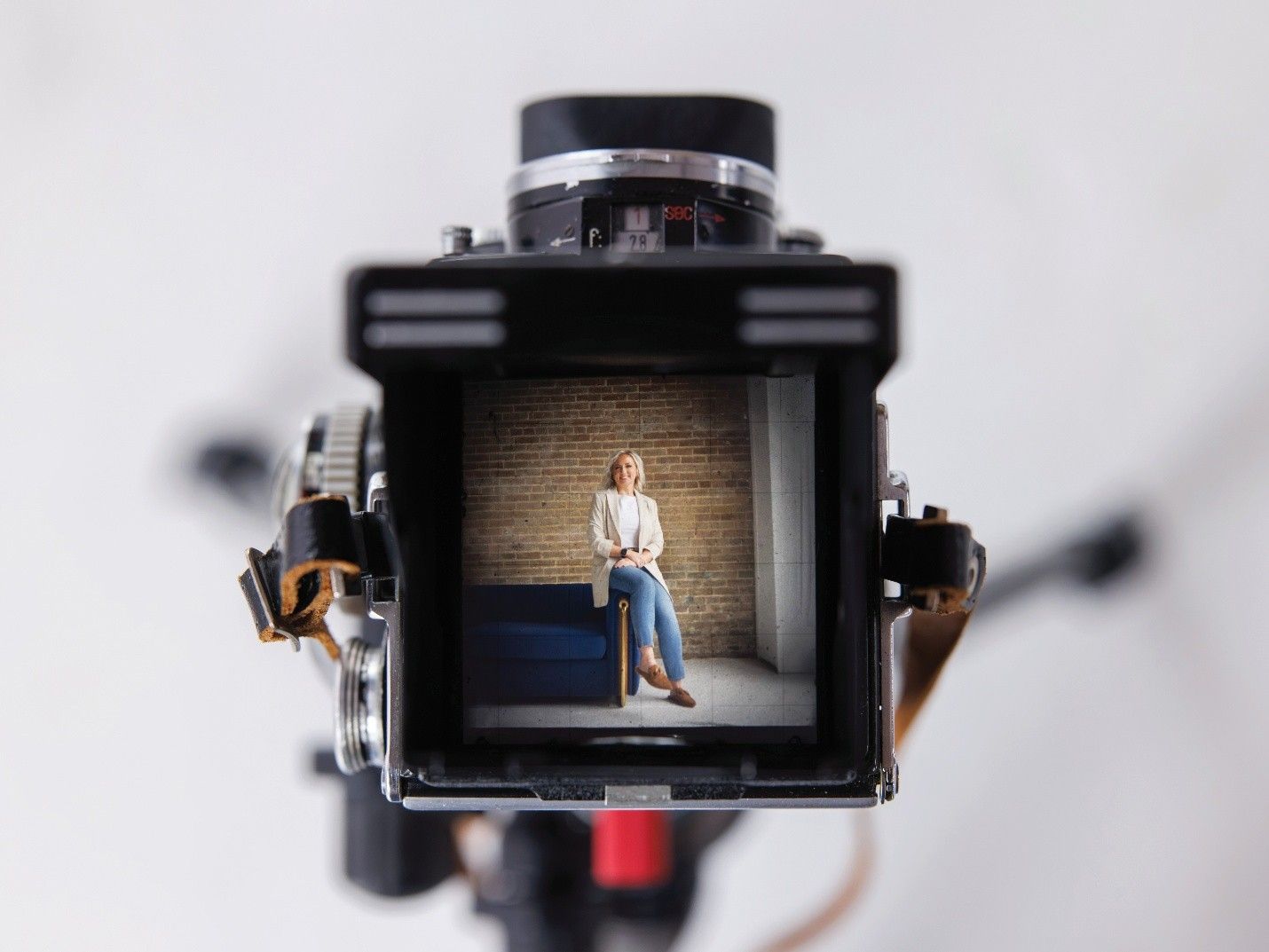 View through vintage camera; woman sitting in a room, brown brick wall.