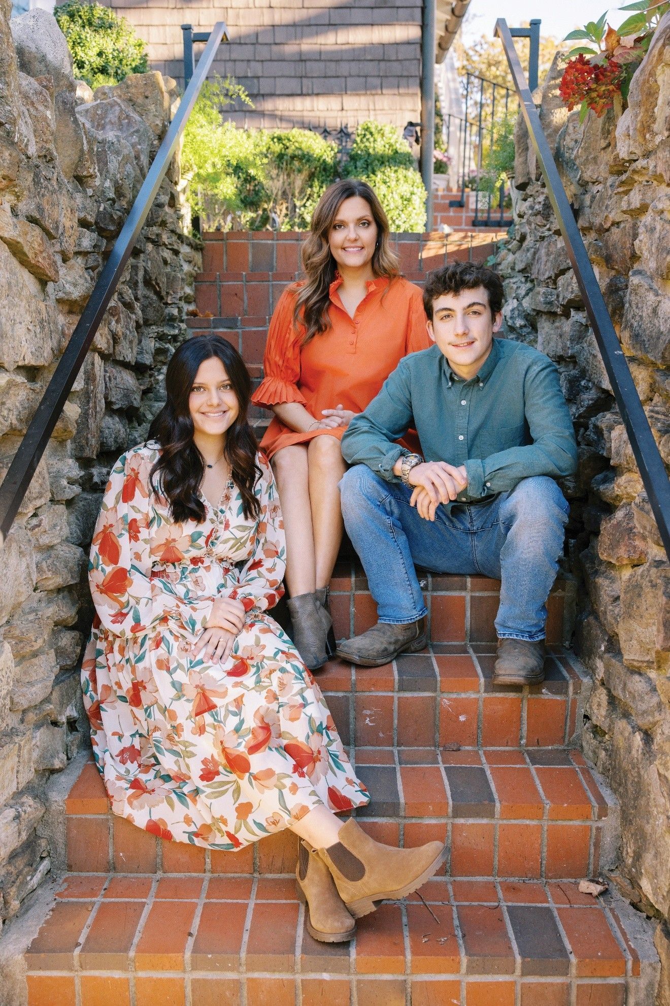 Three people sitting on brick steps. Woman in orange shirt, girl in floral dress, and boy in green shirt.