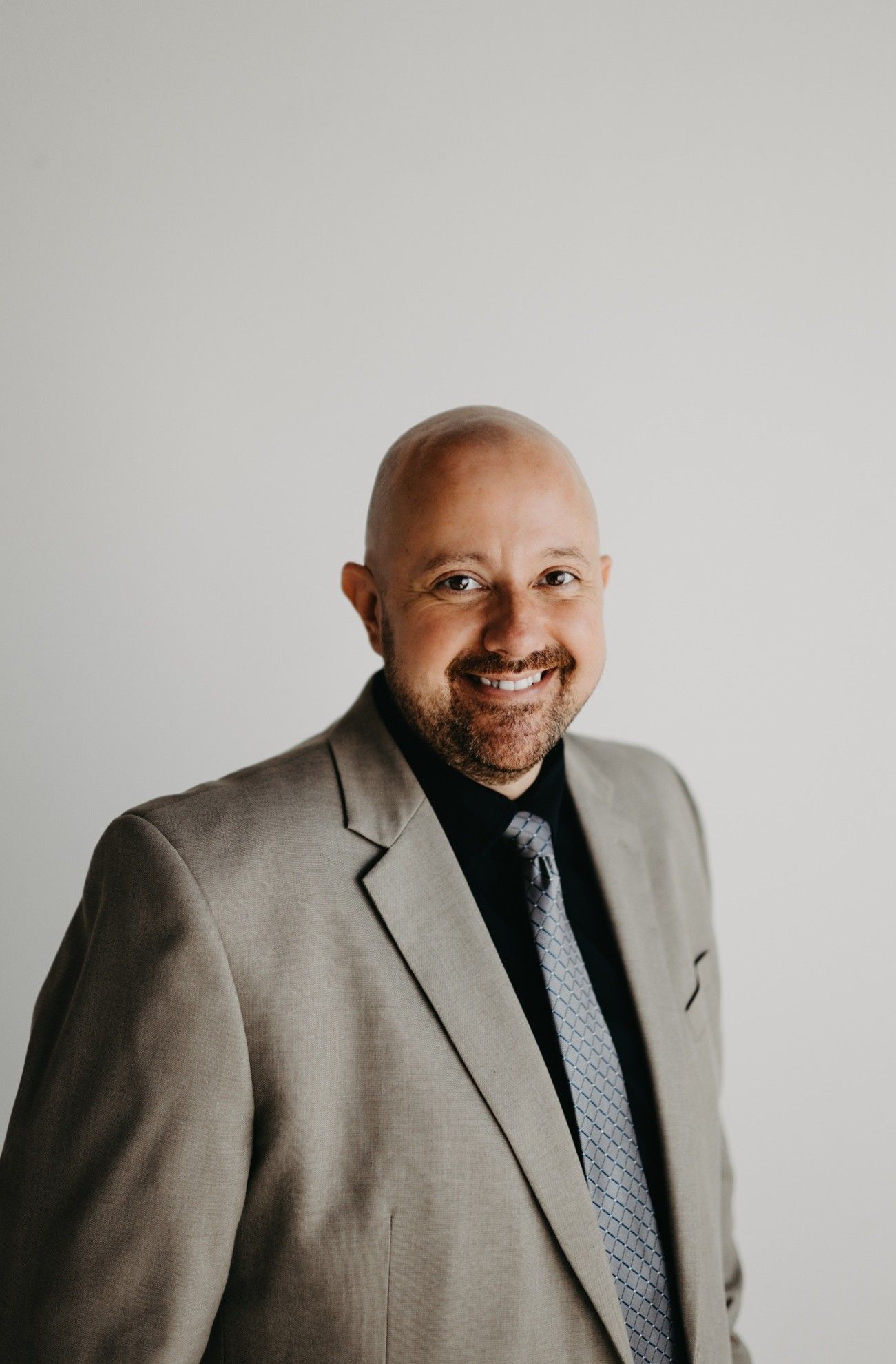 Man in a gray suit smiles at the camera, against a white background.