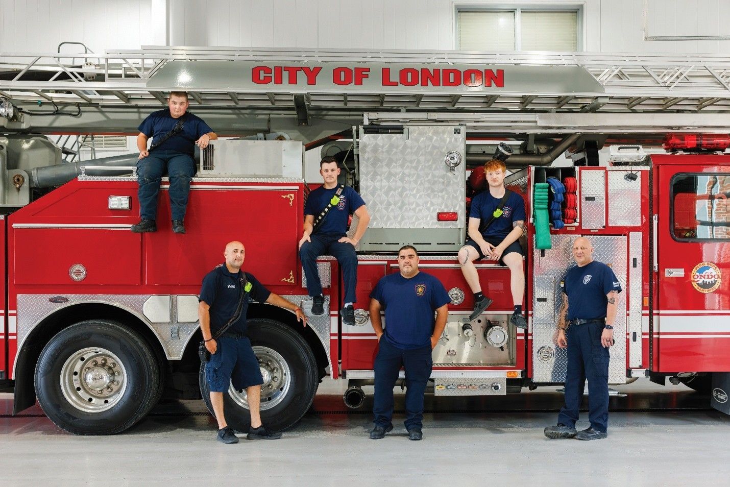 Firefighters posing in front of a City of London fire truck, red and silver, in a garage.