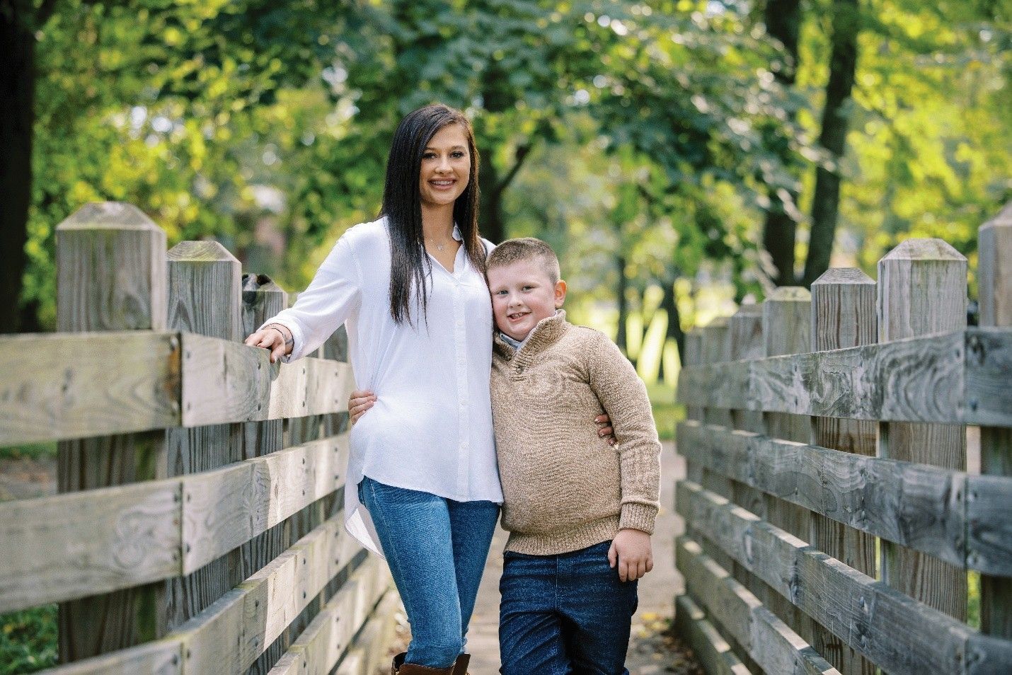 Woman and boy on a wooden bridge. Woman in white shirt and jeans, boy in sweater and dark pants. Trees in background.