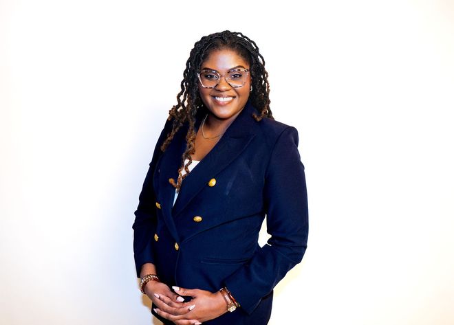 Smiling woman in a navy blazer with gold buttons, standing against a white background.