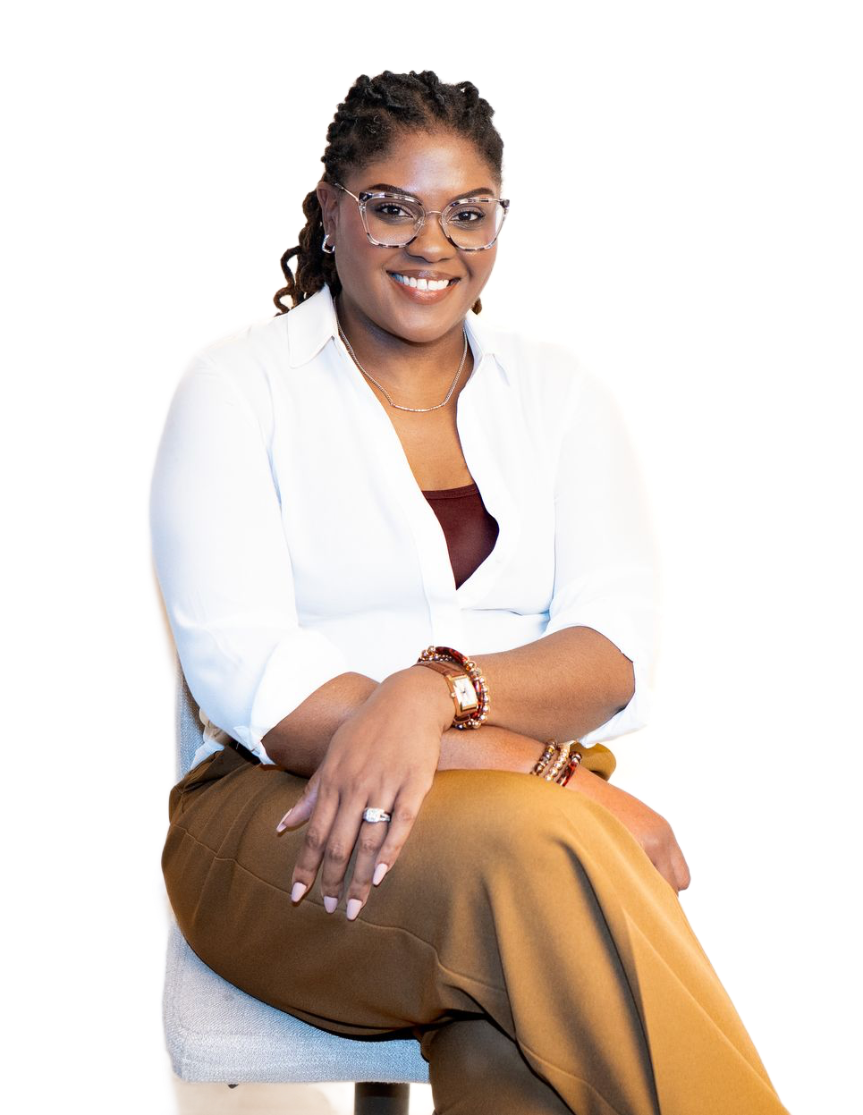Smiling person seated on a stool, wearing a white top and tan pants on a plain white background