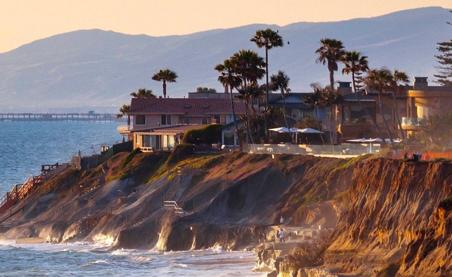 A house sits on top of a cliff overlooking the ocean.