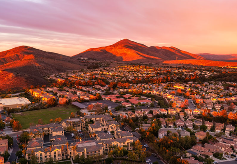 An aerial view of a residential area at sunset with mountains in the background.