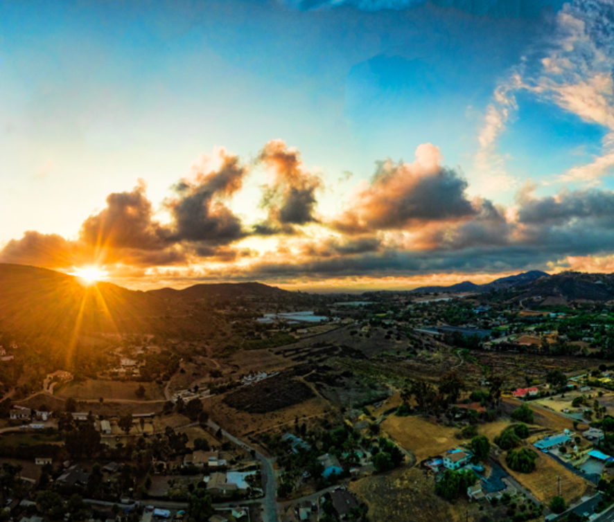 An aerial view of a city at sunset with the sun shining through the clouds.