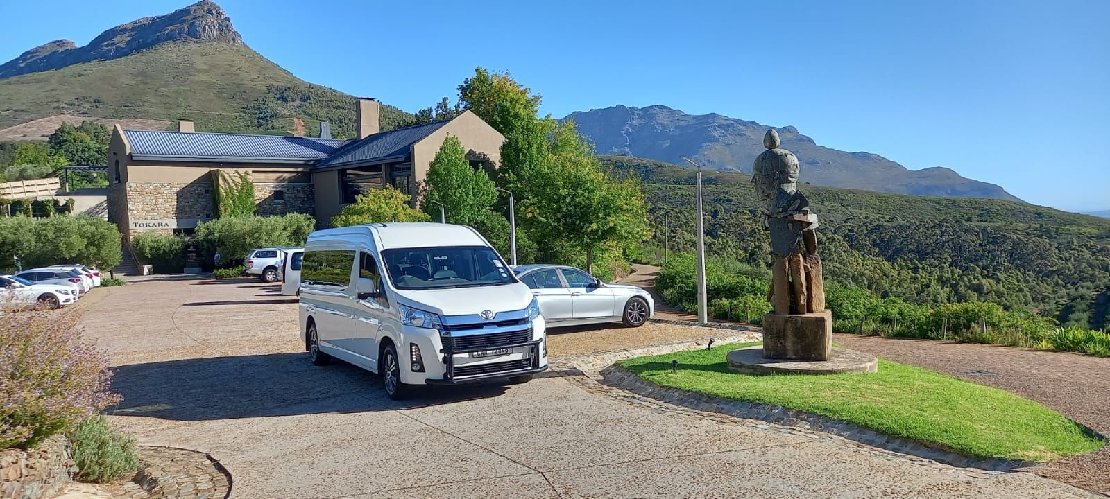 A white van is parked in front of a building with mountains in the background.