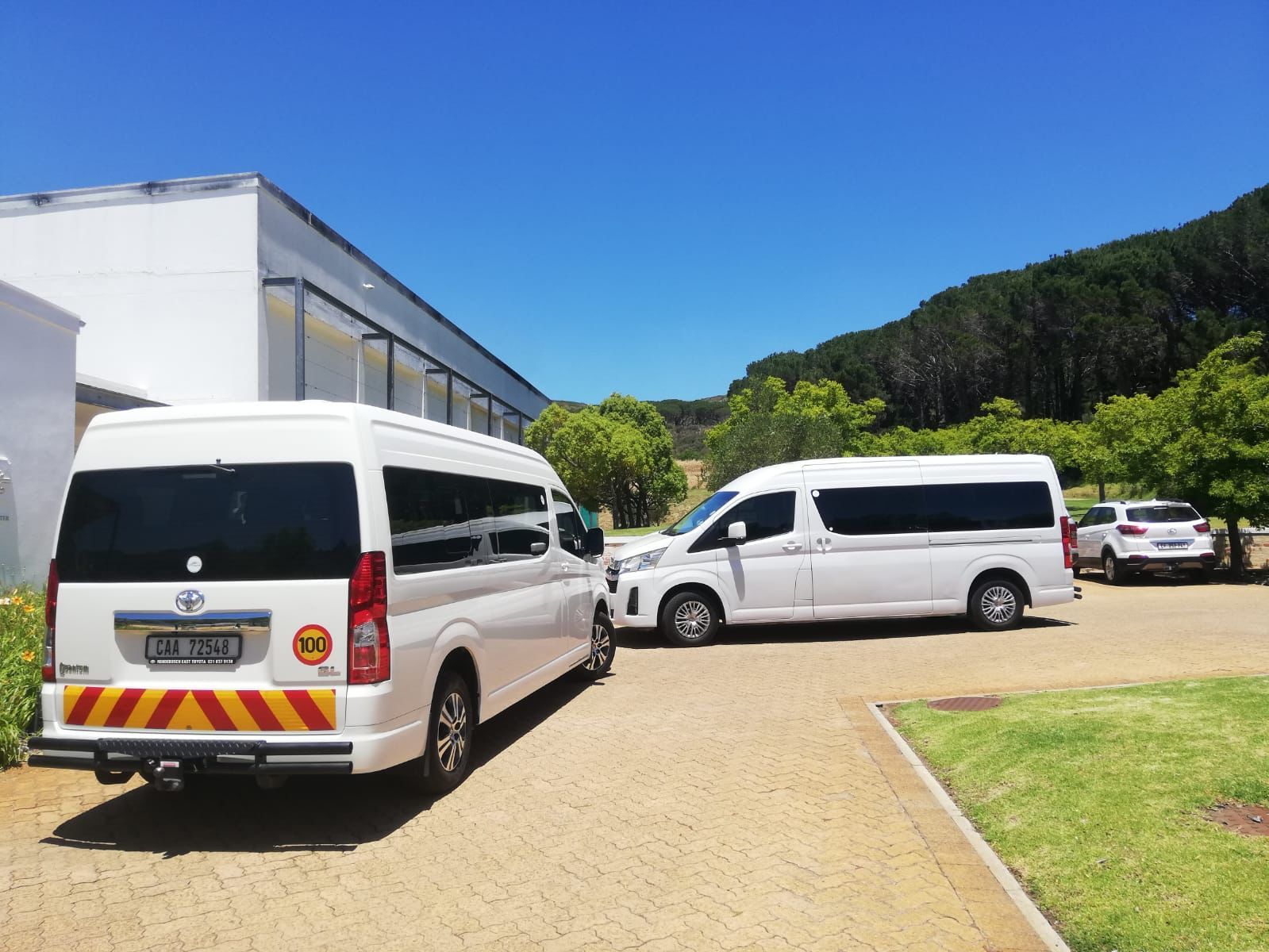 Three white vans are parked in a driveway in front of a building.