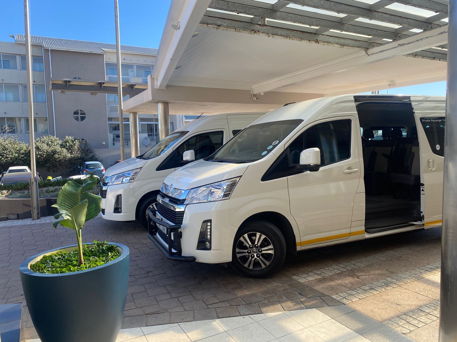 Two white vans are parked under a canopy in front of a building.