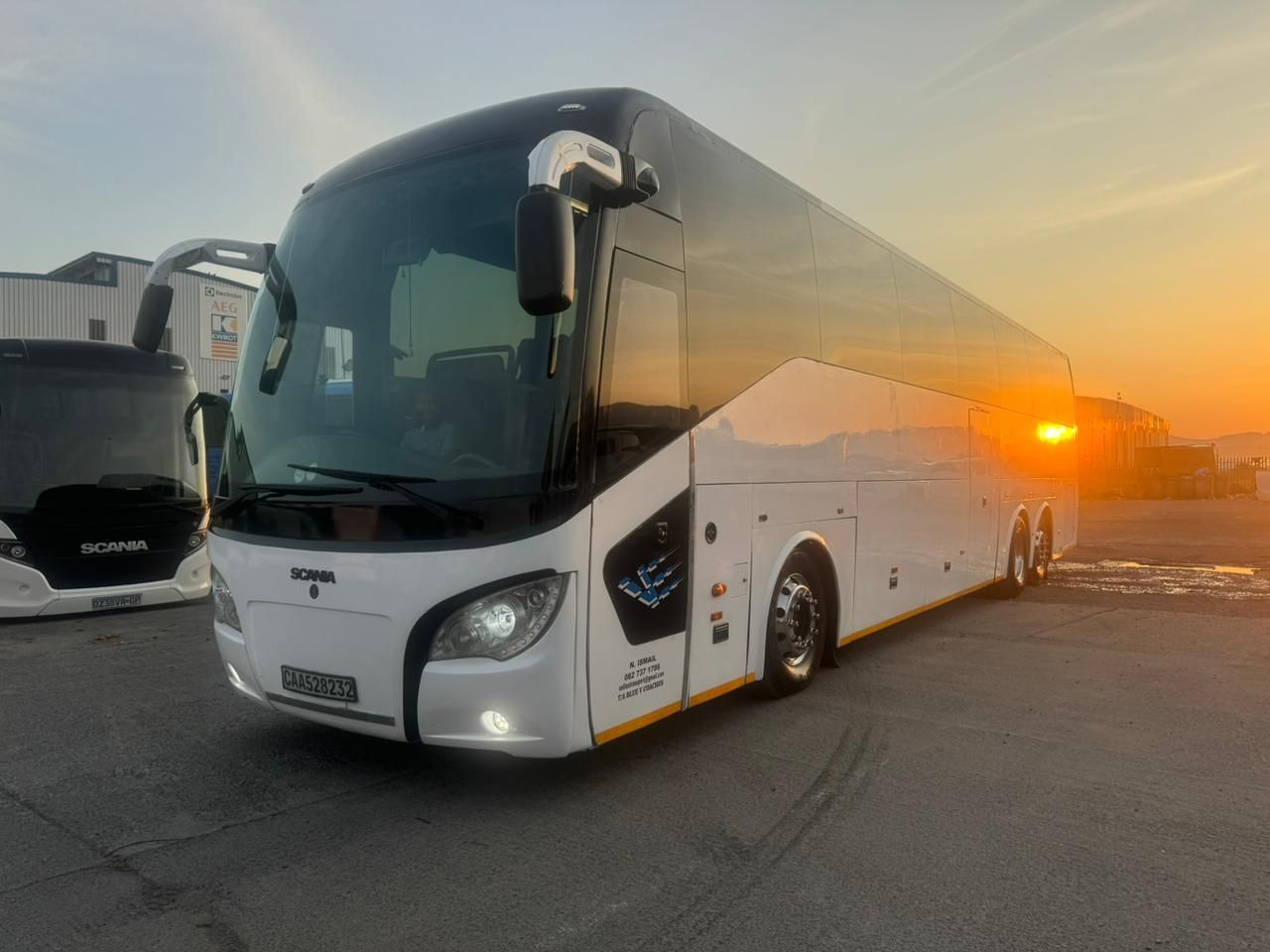 A large white bus is parked in a parking lot at sunset.