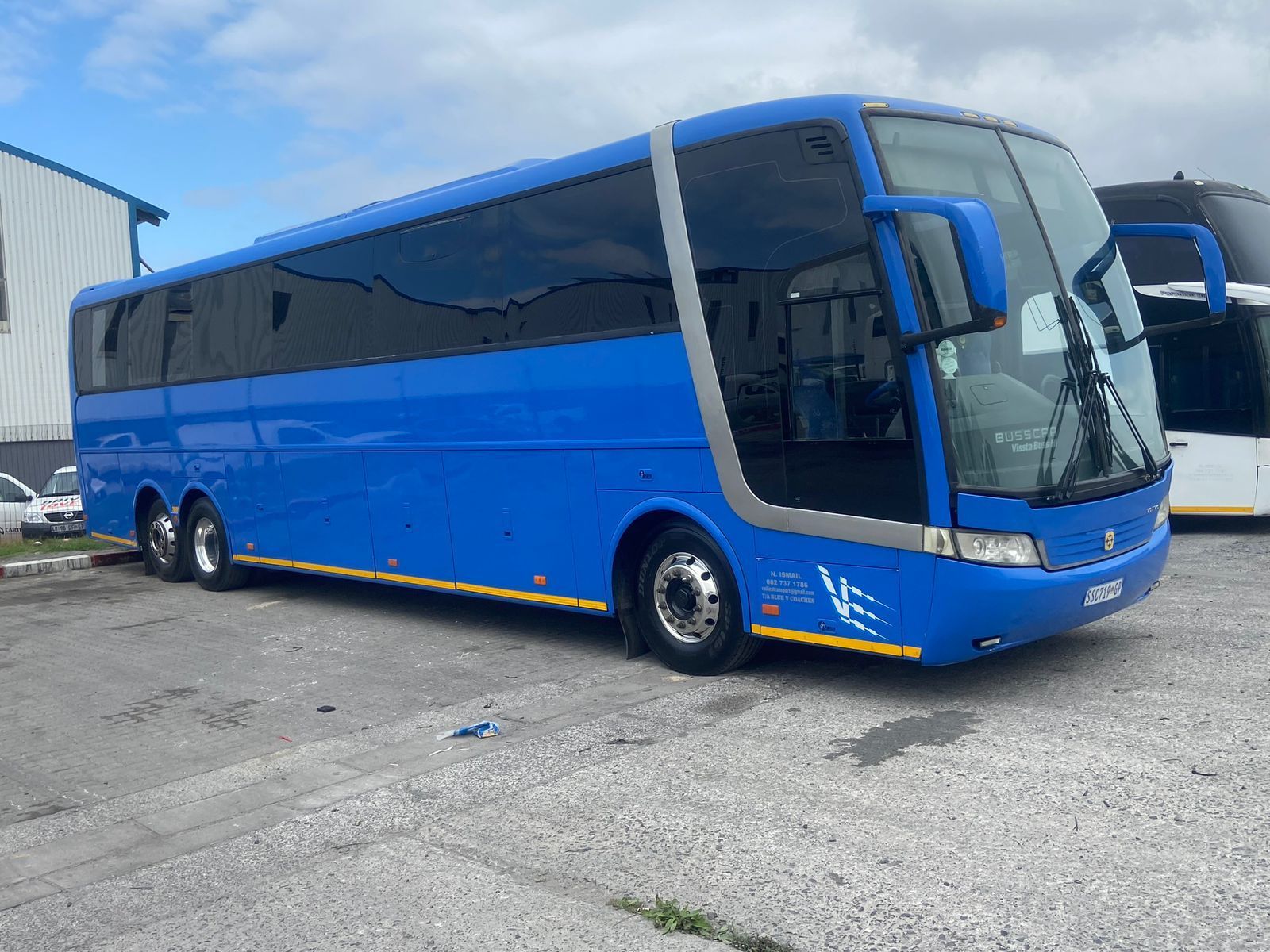 A blue bus is parked in a gravel lot.