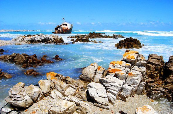 A boat is sitting on top of a rocky beach near the ocean.