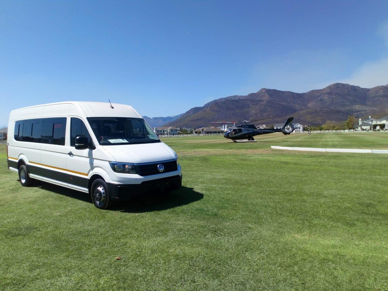 A white van is parked in a grassy field next to a helicopter.