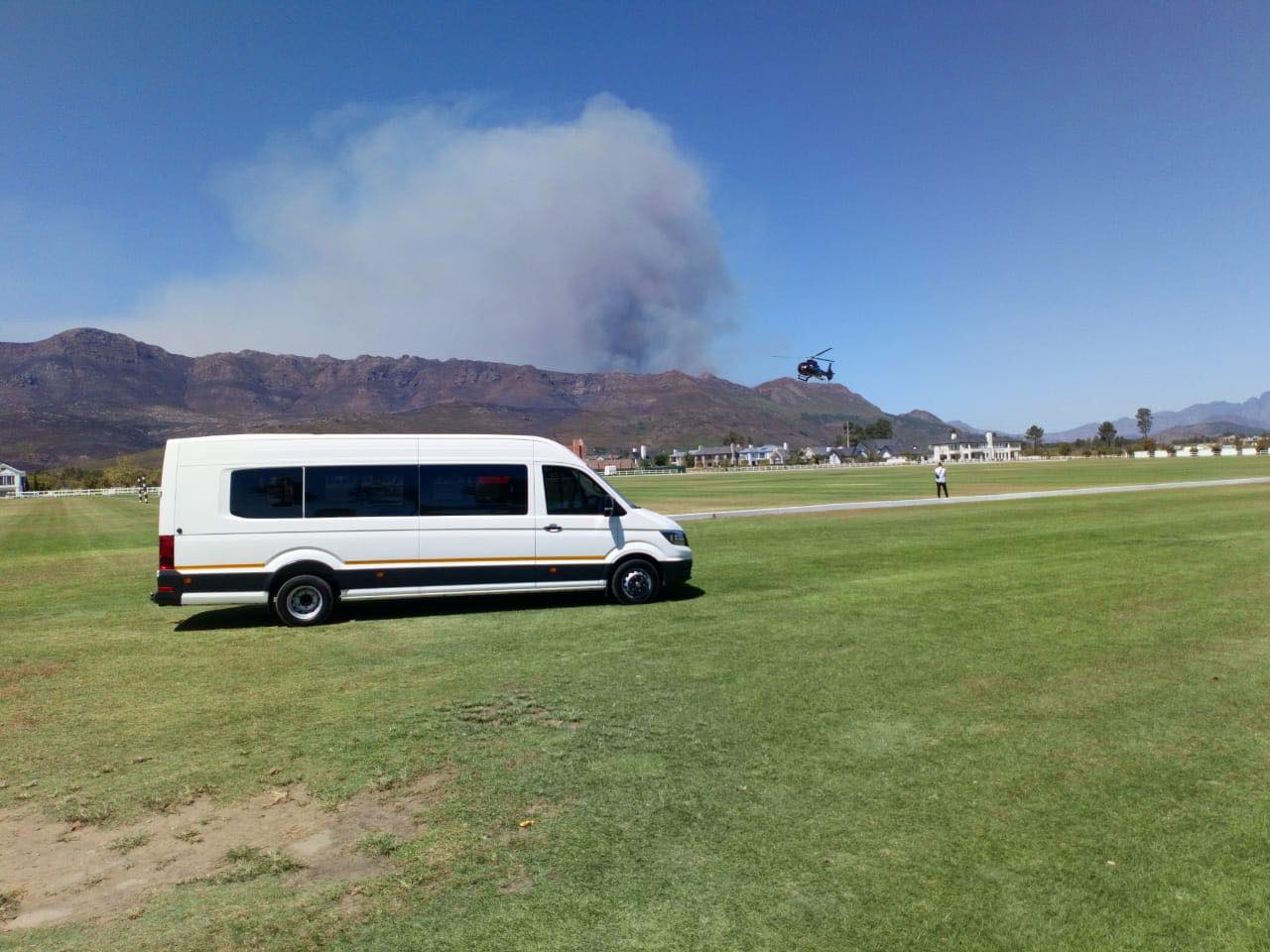 A white van is parked in a grassy field with a mountain in the background.