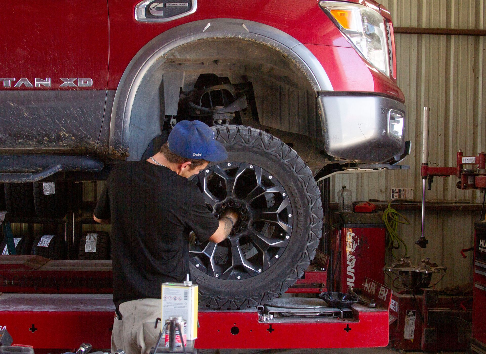 Mechanic changing a tire on a red truck in a garage. Man in a blue cap works on the wheel.