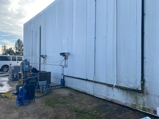 A white building with a lot of pipes and a van parked in front of it.