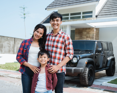 Family of three standing outside a house beside a black SUV, smiling at the camera.