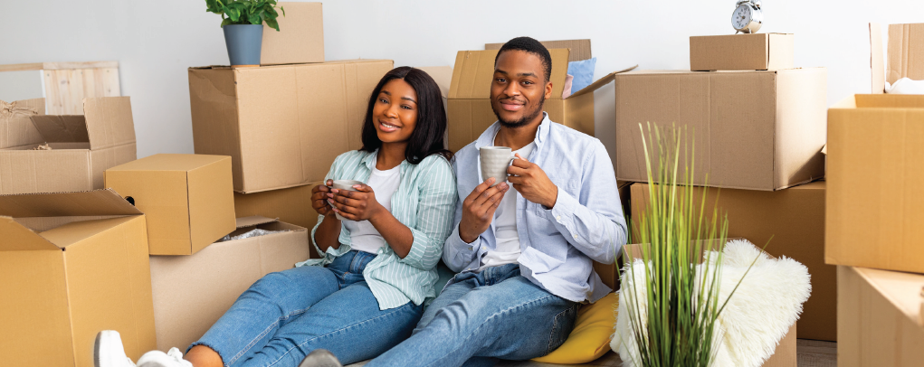 Couple sitting among moving boxes in a new home, smiling and clapping on the floor