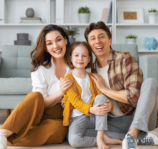 A smiling family of three sits on the floor together in a bright, modern living room.