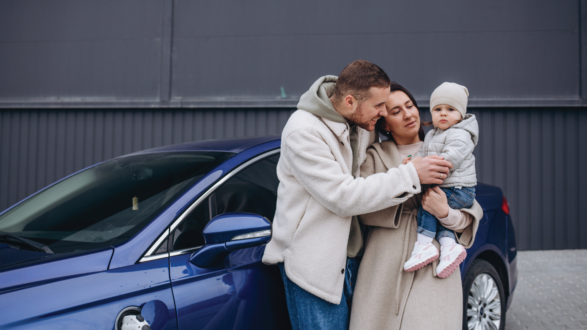 Family standing beside a blue car, sharing a warm embrace outdoors