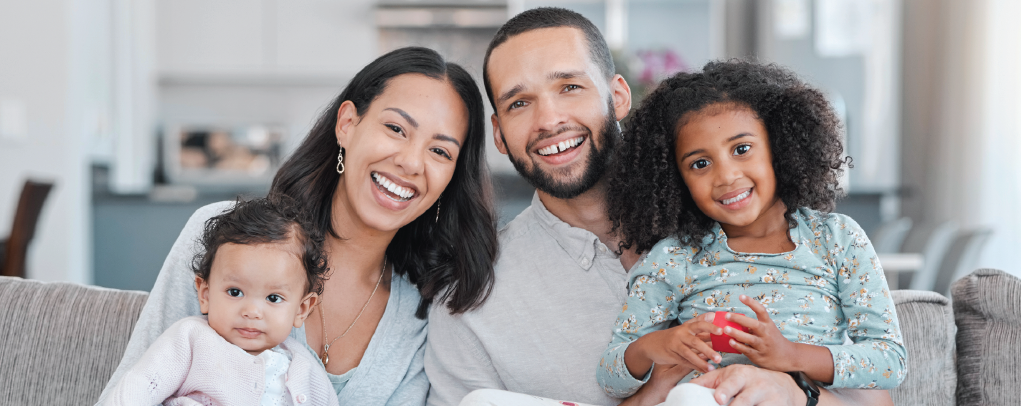 Family of four smiling on a couch in a bright living room